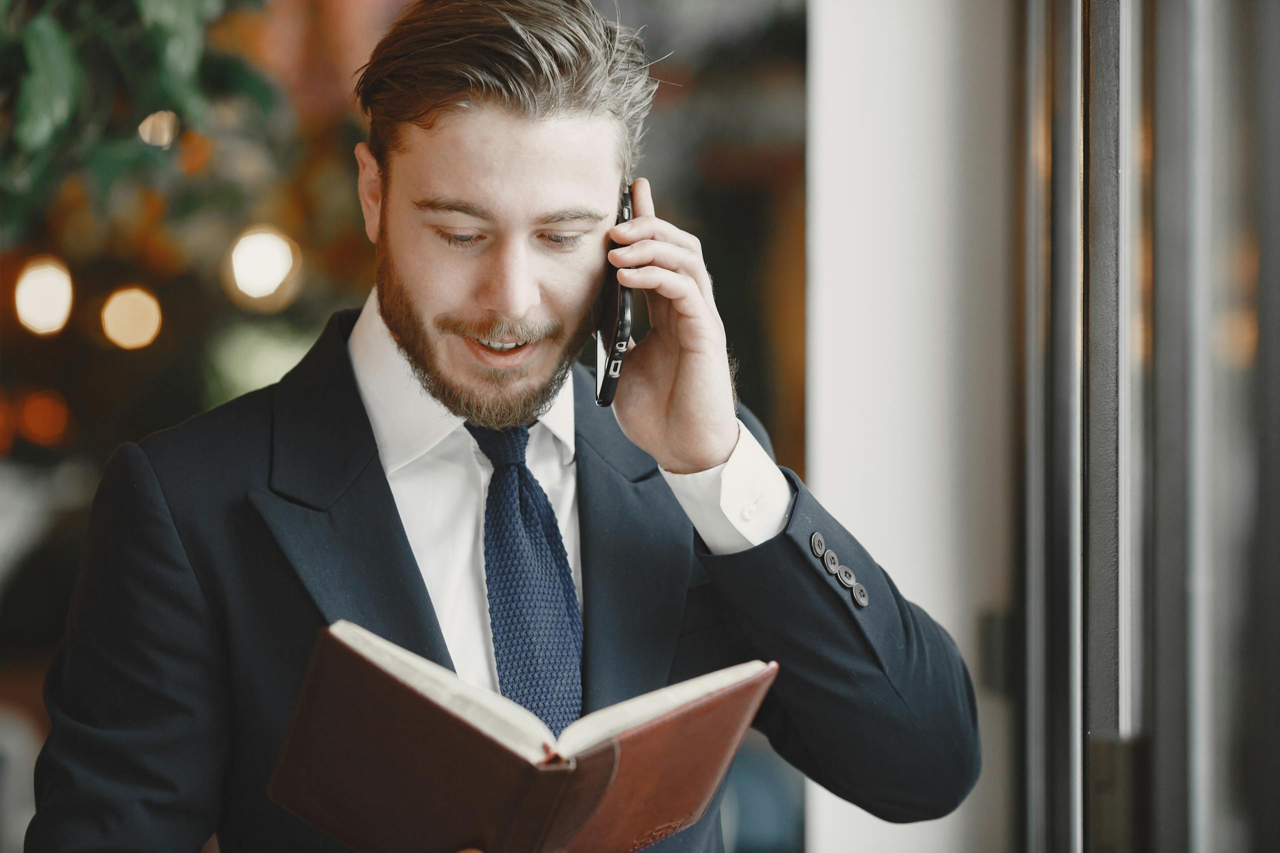 A professional businessman in a suit having a phone call while holding a book.